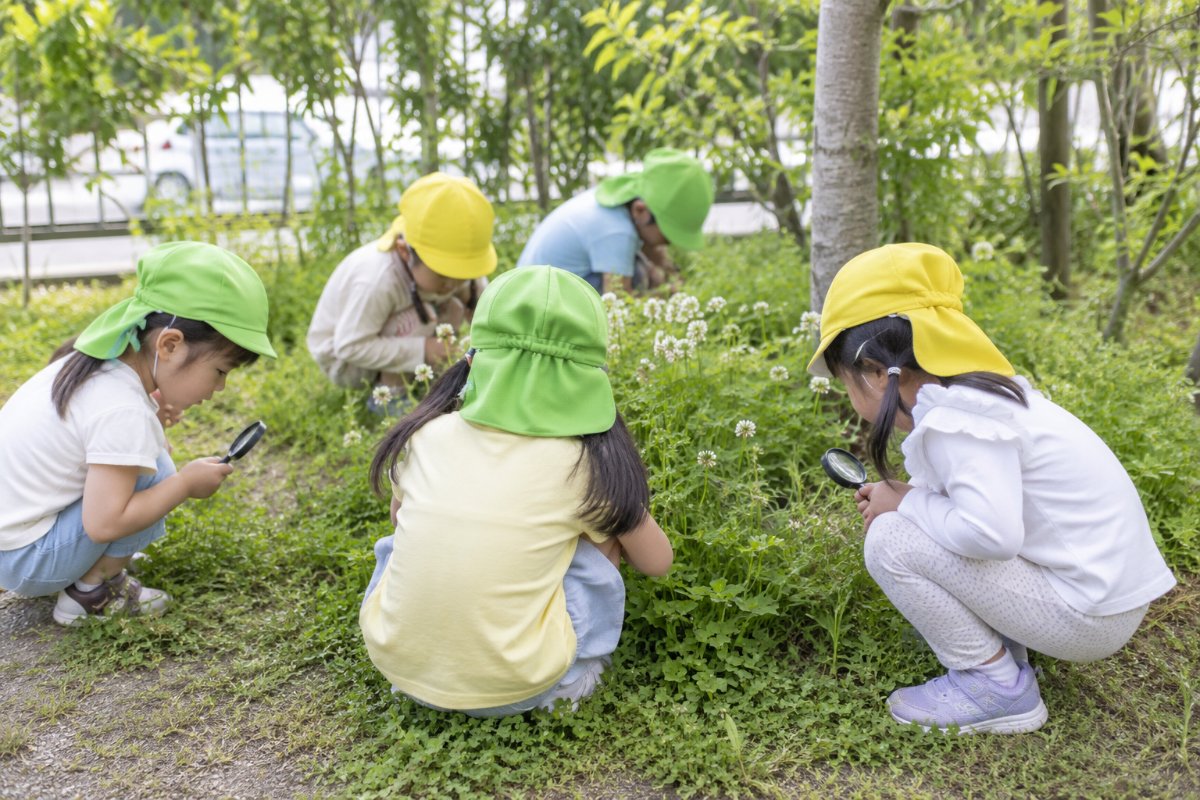 園庭で虫めがねをのぞく子どもたち